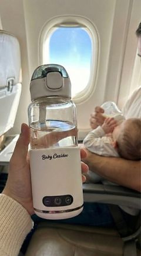 Le chauffe-biberon sans fil Babycozidoo posé devant le hublot d'un avion, bébé dans les bras à l'arrière