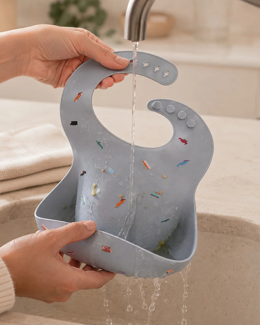 Bavoir en silicone rincé sous un filet d'eau au-dessus d'un évier