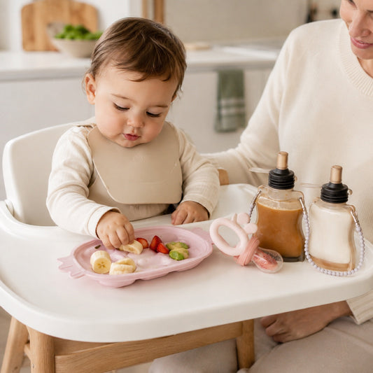 Bébé attablé dans sa chaise haute avec une assiette et des accessoires repas en silicone devant lui