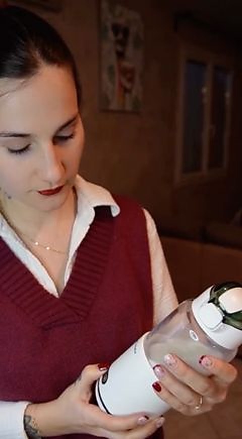 Une jeune femme tient le chauffe-biberon sans fil Babycozidoo dans son salon