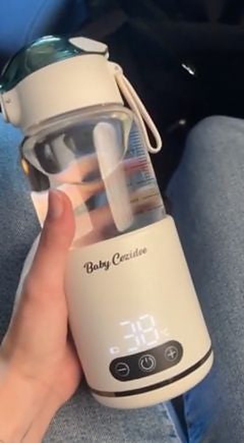 Le chauffe-biberon sans fil Babycozidoo tenu en main dans la voiture, écran de température allumé