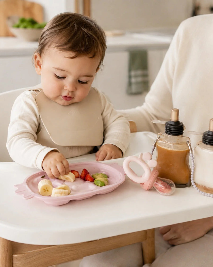 Bébé installé en chaise haute avec le set repas silicone, cuisine lumineuse
