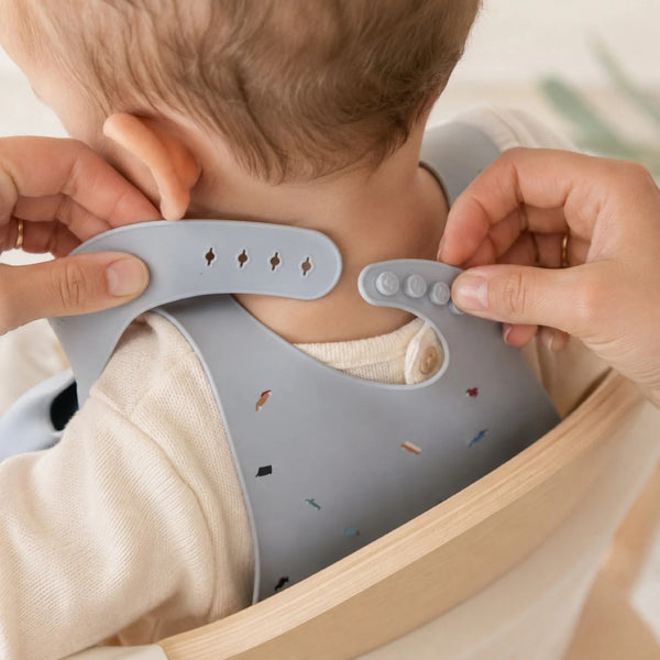 Mains ajustant la fermeture du bavoir en silicone autour du cou de bébé