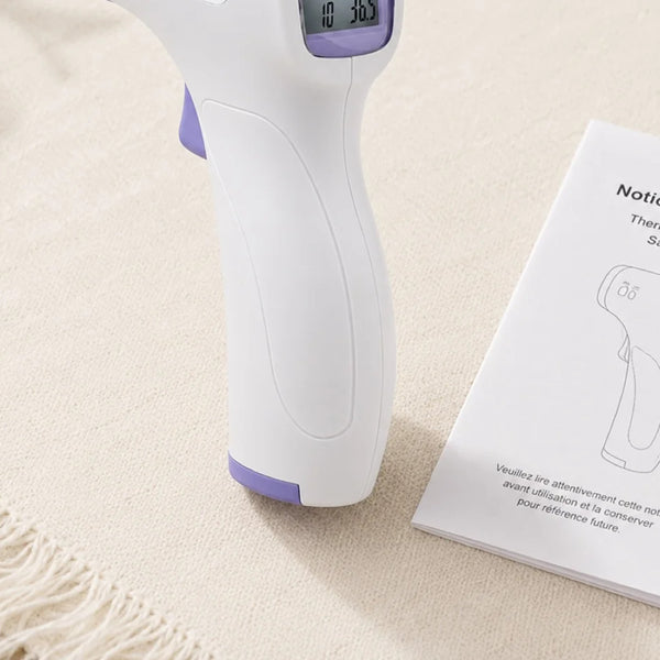 Thermomètre frontal sans contact posé à côté de sa notice d'utilisation