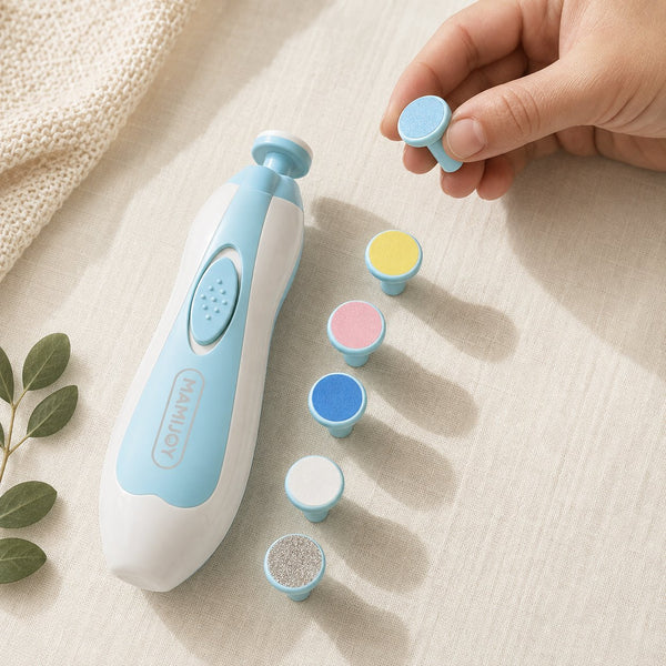 Coupe-ongles électrique pour bébé posé sur un tissu écru avec ses six embouts de limage de grains différents