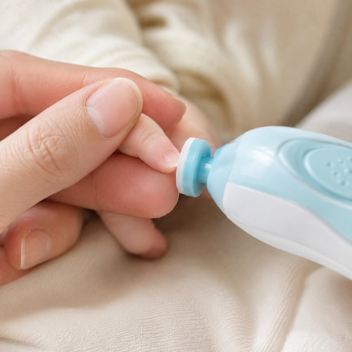 Gros plan sur l'embout du coupe-ongles électrique posé sur l'ongle d'un doigt de bébé tenu entre deux doigts