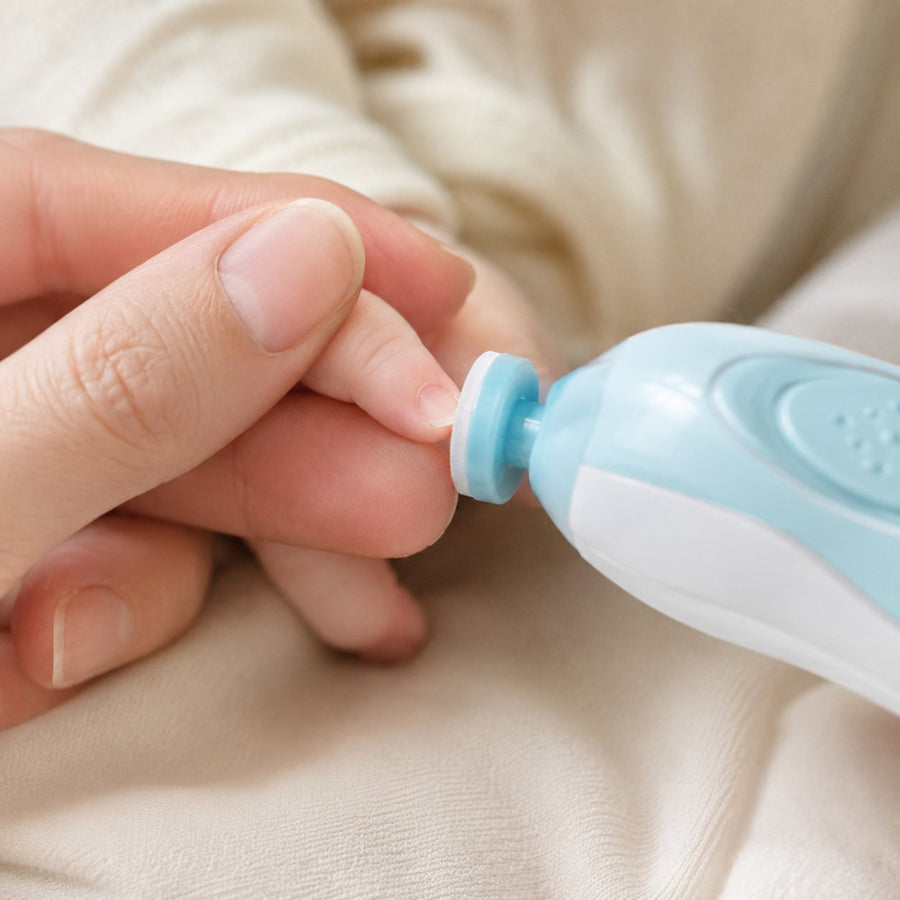 Gros plan sur l'embout du coupe-ongles électrique posé sur l'ongle d'un doigt de bébé tenu entre deux doigts