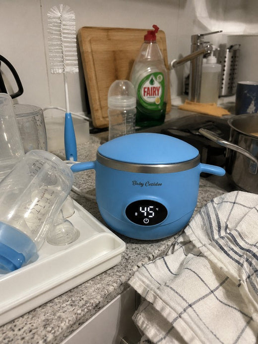 Un Babycozidoo bleu sur le plan de travail de la cuisine, au milieu des biberons en train de sécher