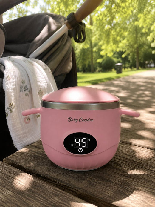 Un Babycozidoo rose sur une table de pique-nique dans un parc, la poussette garée à côté